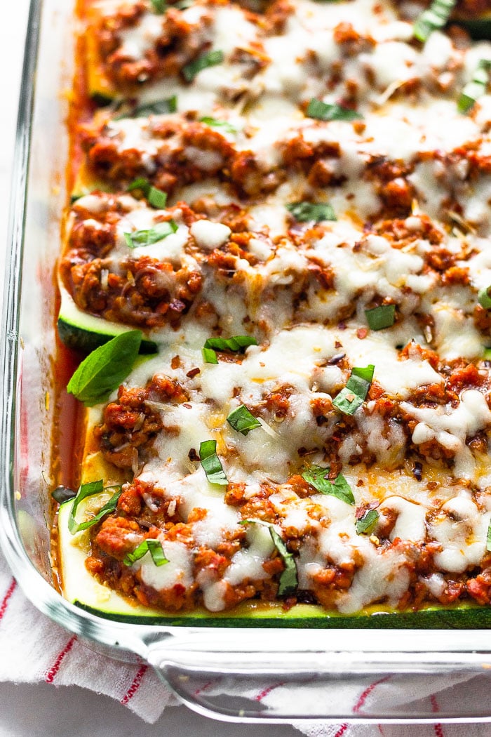 Close up of low carb zucchini pizza boats in a glass baking dish topped with fresh bail and red pepper flakes.