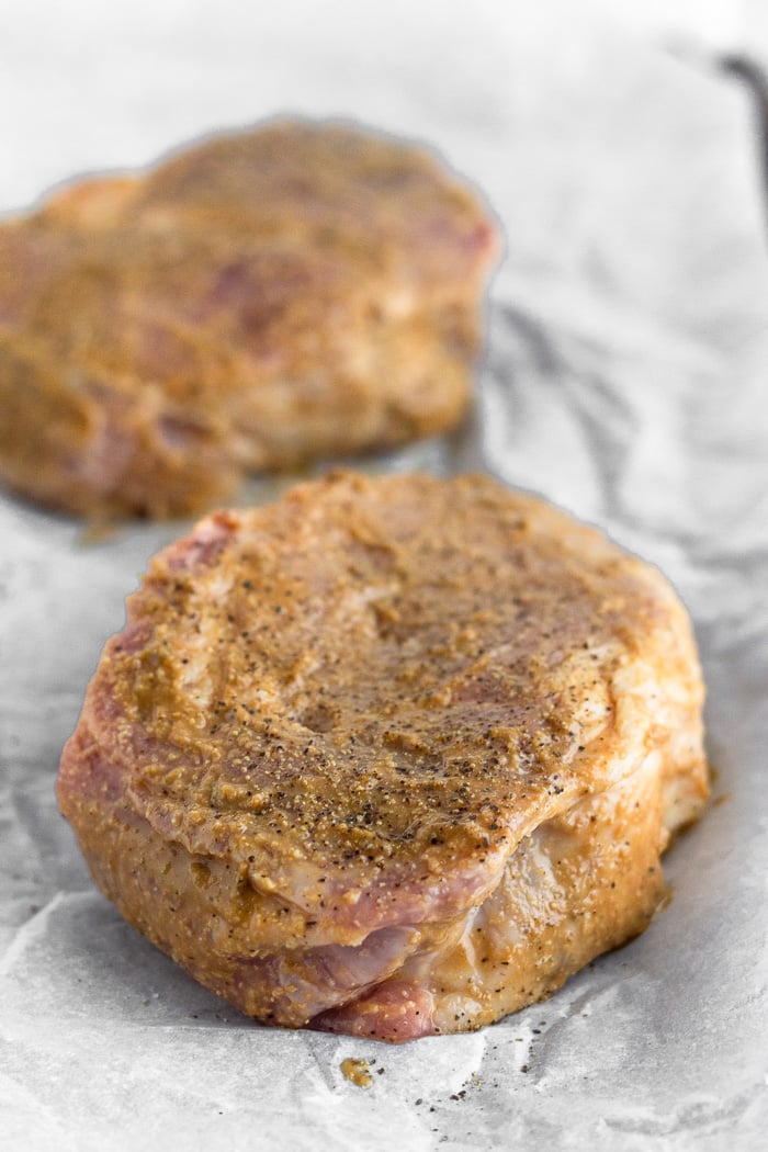 Baking sheet with raw pork chops covered in a balsamic mustard mixture.