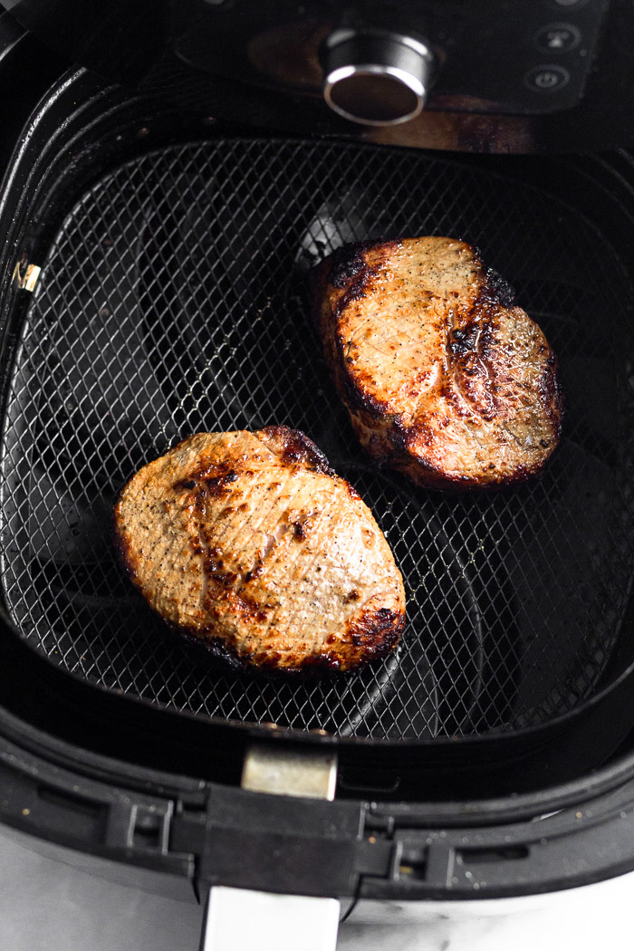 Two cooked pork chops in an air fryer basket.