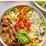 Overhead shot of a chicken burrito bowl with cilantro lime rice, shredded cheese, corn, black beans, guacamole, sliced seasoned chicken, lettuce, shredded cheese, fajita veggies, and pico de gallo.