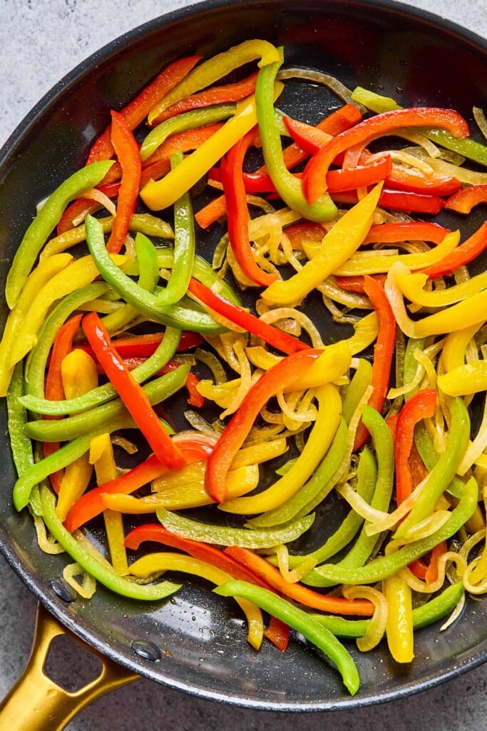 Large skillet with sautéed sliced onions and peppers in it.