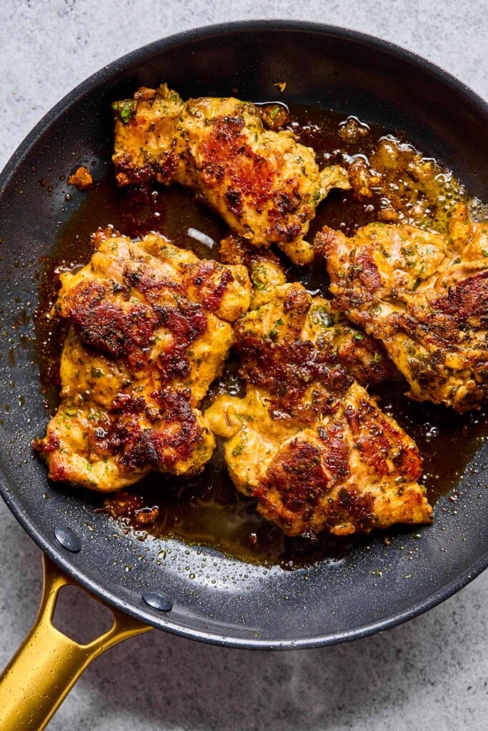 Skillet with seasoned pan fried chicken thighs in it.