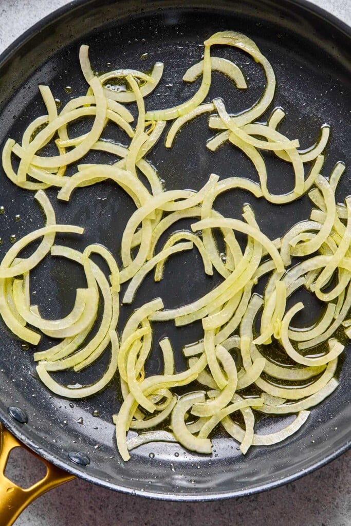 Large skillet with sautéed sliced onions in it.