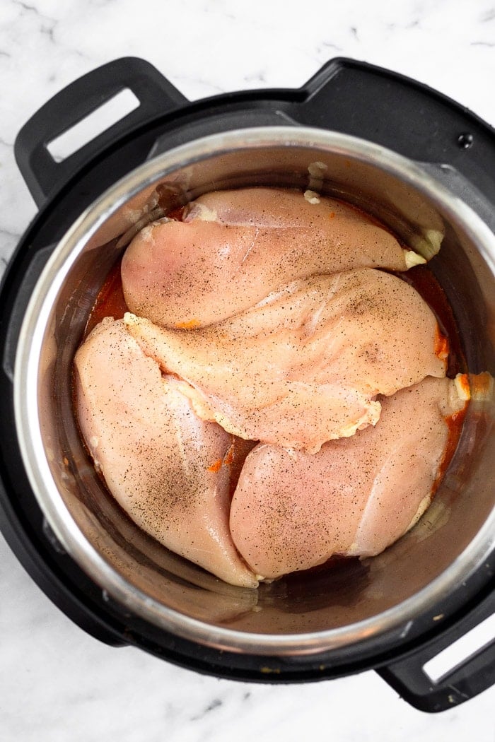 Pressure cooker filled with a little bit of buffalo sauce and 4 raw chicken breasts.