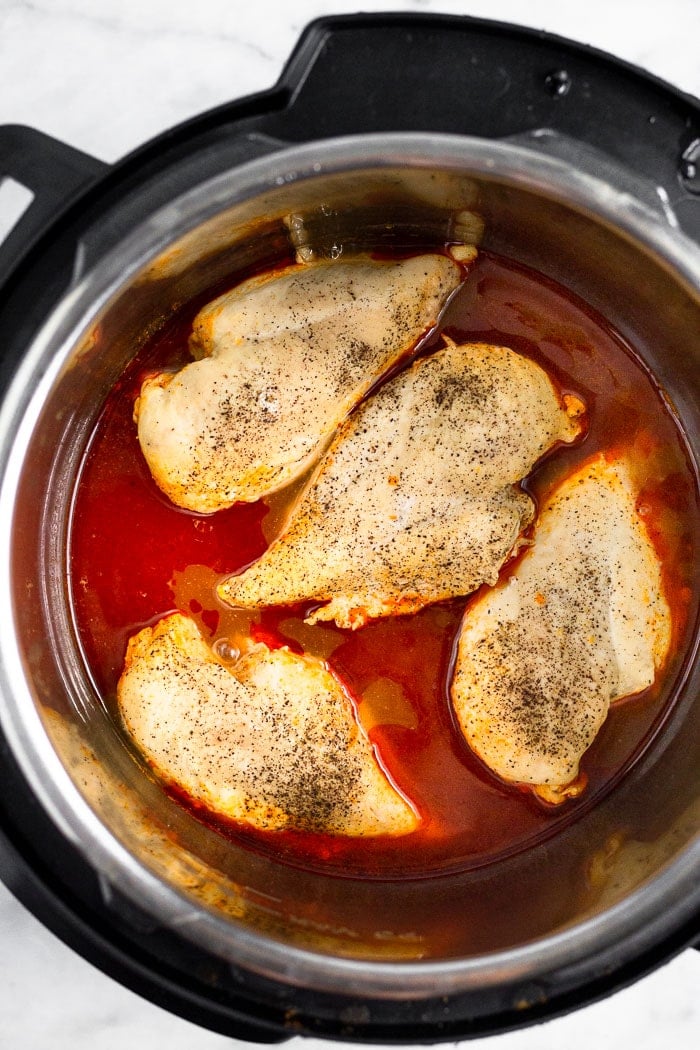Pressure cooker filled with buffalo sauce and 4 cooked chicken breasts.