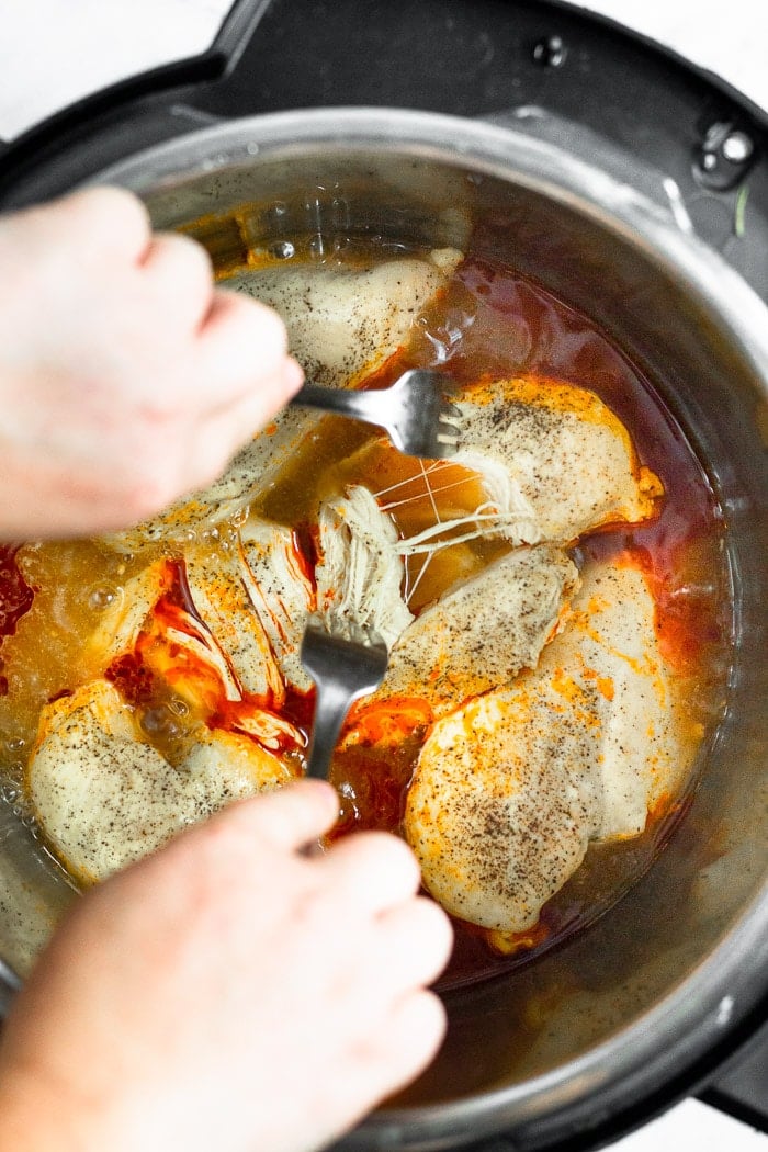 Instant Pot buffalo chicken being shredded with two forks in a pressure cooker.