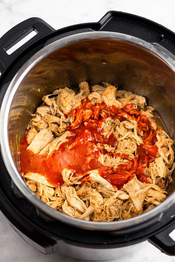 Instant Pot filled with shredded chicken with buffalo sauce poured on top of it.