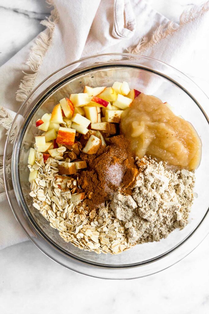 Large glass down with rolled oats, diced apple, applesauce, protein powder, and spices in it.