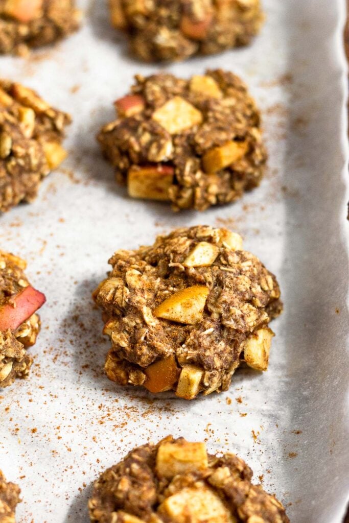 Oatmeal protein cookies on a parchment paper lined baking sheet. They are sprinkled with cinnamon.