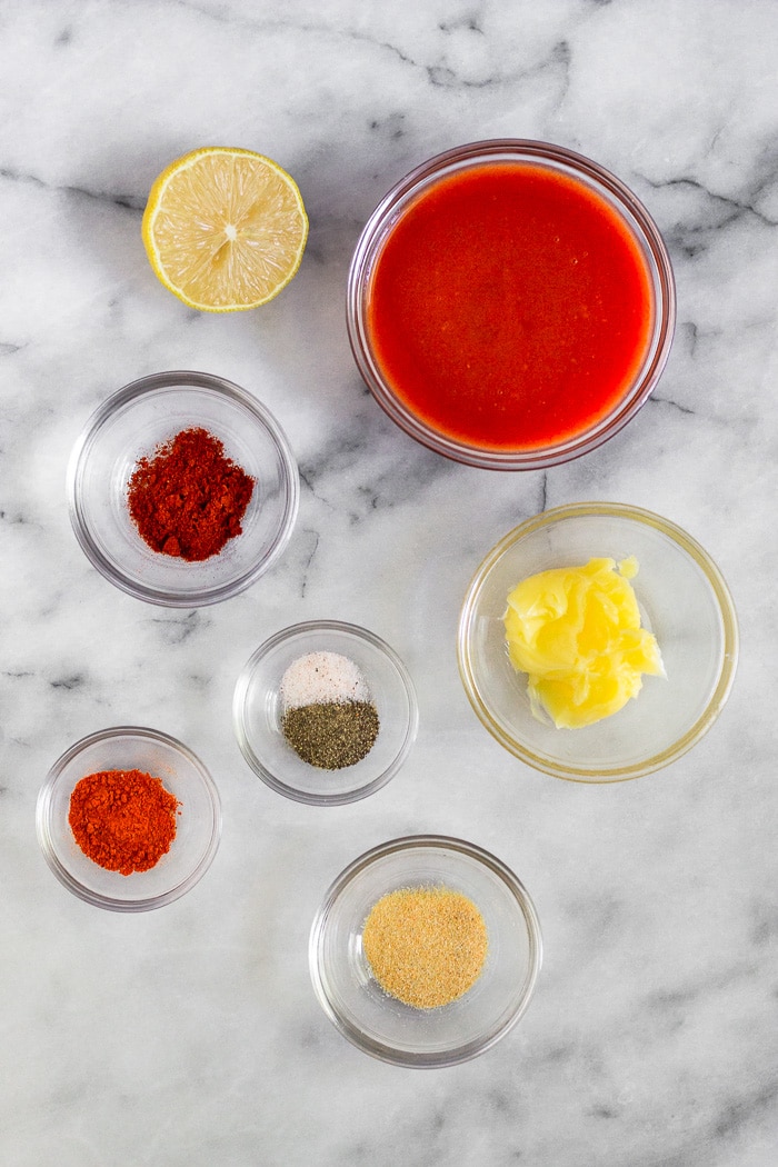 White counter with small bowls of ghee, hot sauce, and spices and half a lemon.