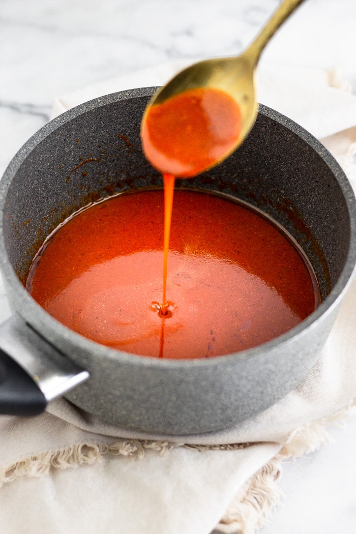 Small sauce pan with homemade buffalo sauce in it with a spoon overtop of it pouring some in.