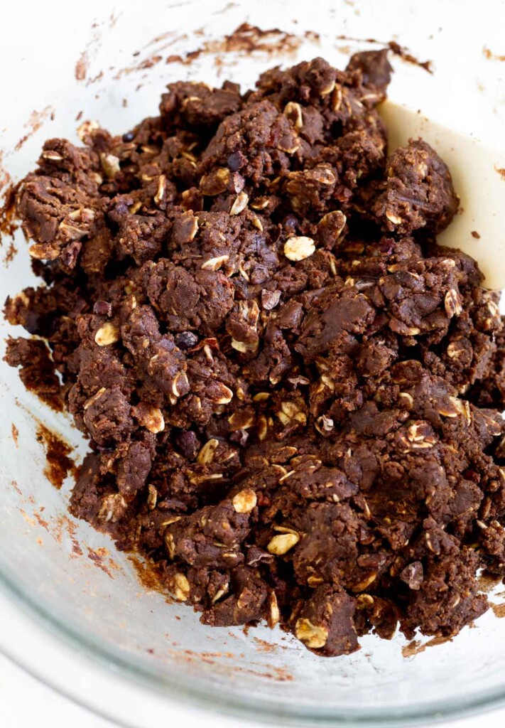 A thick chocolate batter with rolled oats and cacao nibs in it in a large glass bowl.