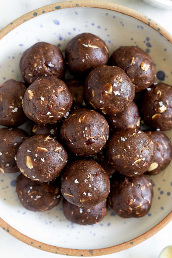 An overhead shot of chocolate energy balls with oats sprinkled with flaky sea salt in a large bowl.