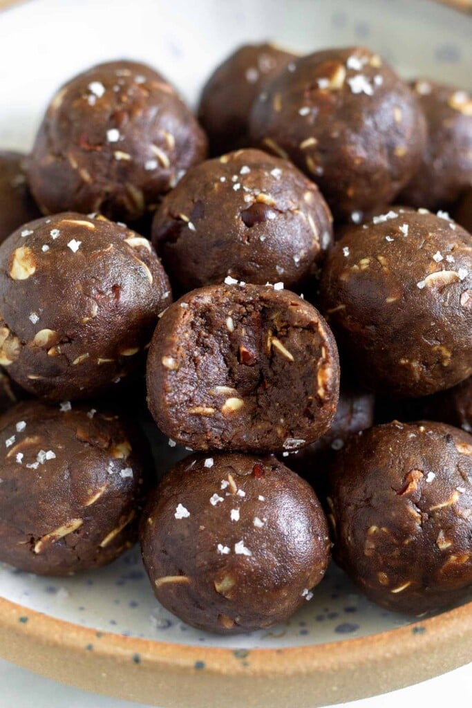 A bowl of peanut butter chocolate protein balls piled on top of each other. One of the protein balls in the front has a bite taken out of it.