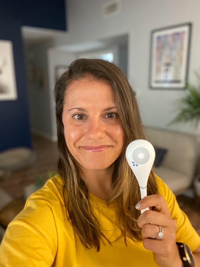 Girl in a yellow shirt with brown hair taking a selfie holding a Dasys Fertility Tracker.