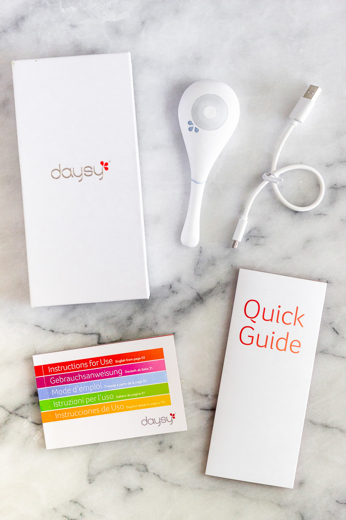 Daysy box, Daysy fertility monitor, charging cord, quick guide, and the Daysy manual on a white counter top.