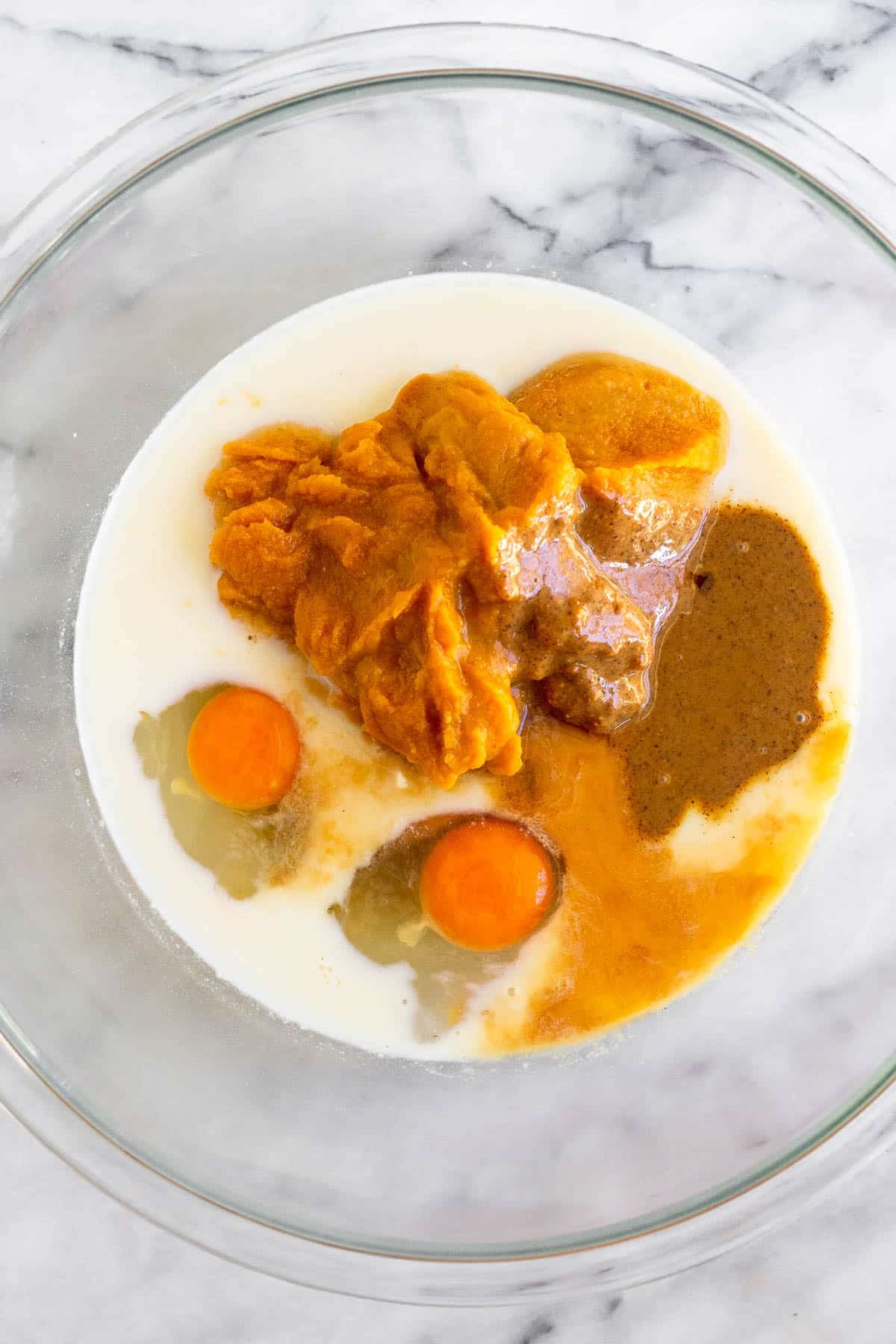 Large glass bowl filled with pumpkin puree, eggs, milk, almond butter, and vanilla extract.