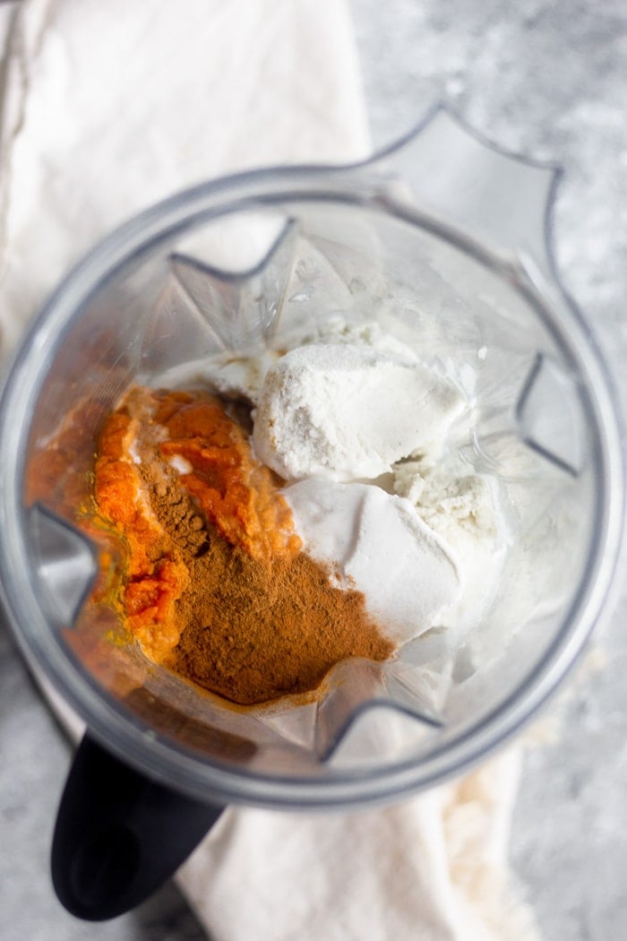 Overhead shot of a blender filled with vanilla ice cream, pumpkin puree, and spices.