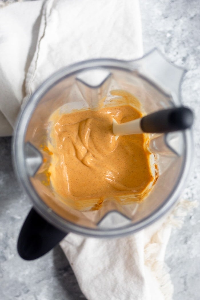 Pumpkin milkshake in a blender with a spatula in it.
