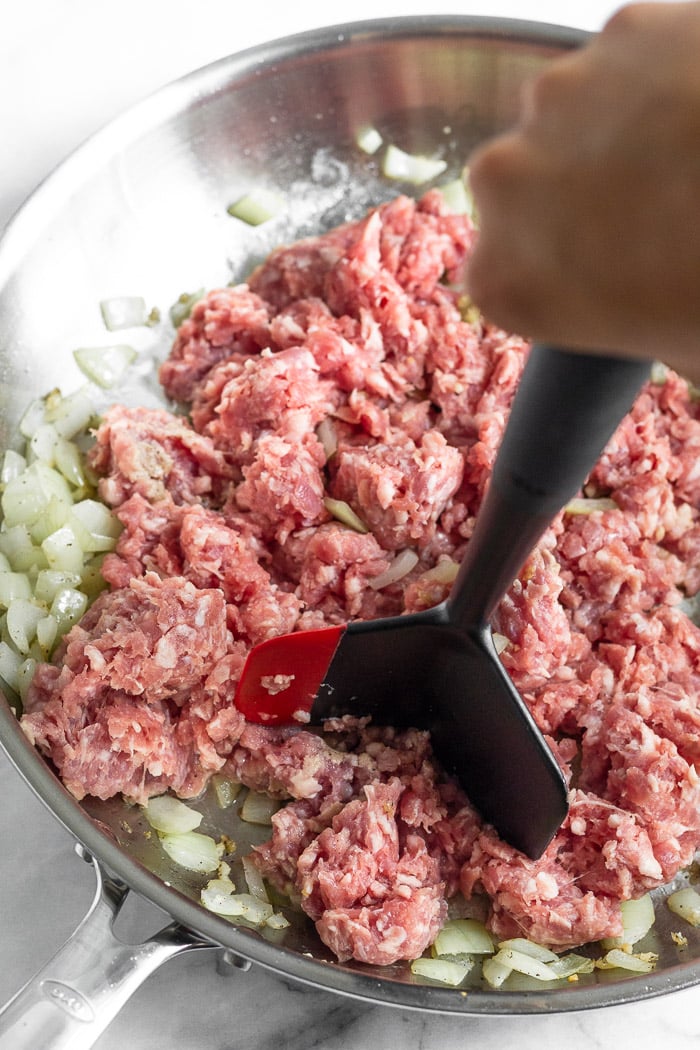 Sauteed onions with raw ground pork in a large pan with a meat chopper breaking it up.