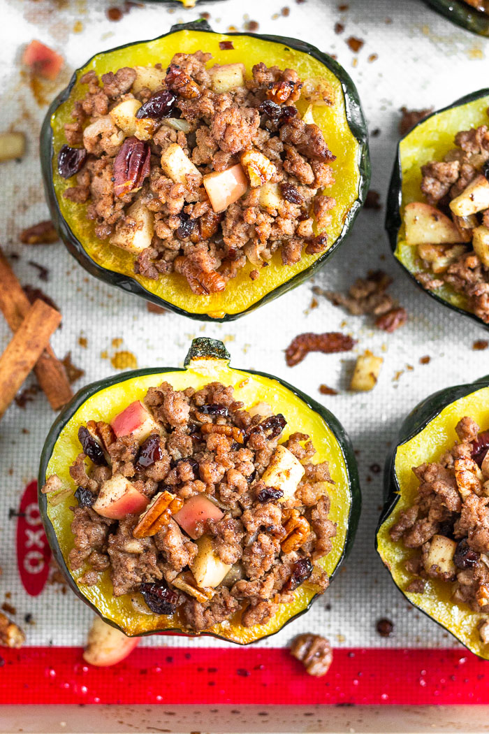 Overhead shot of stuffed acorn squash filled sausage and apples on a baking sheet. The filling is also scattered around the squashes.