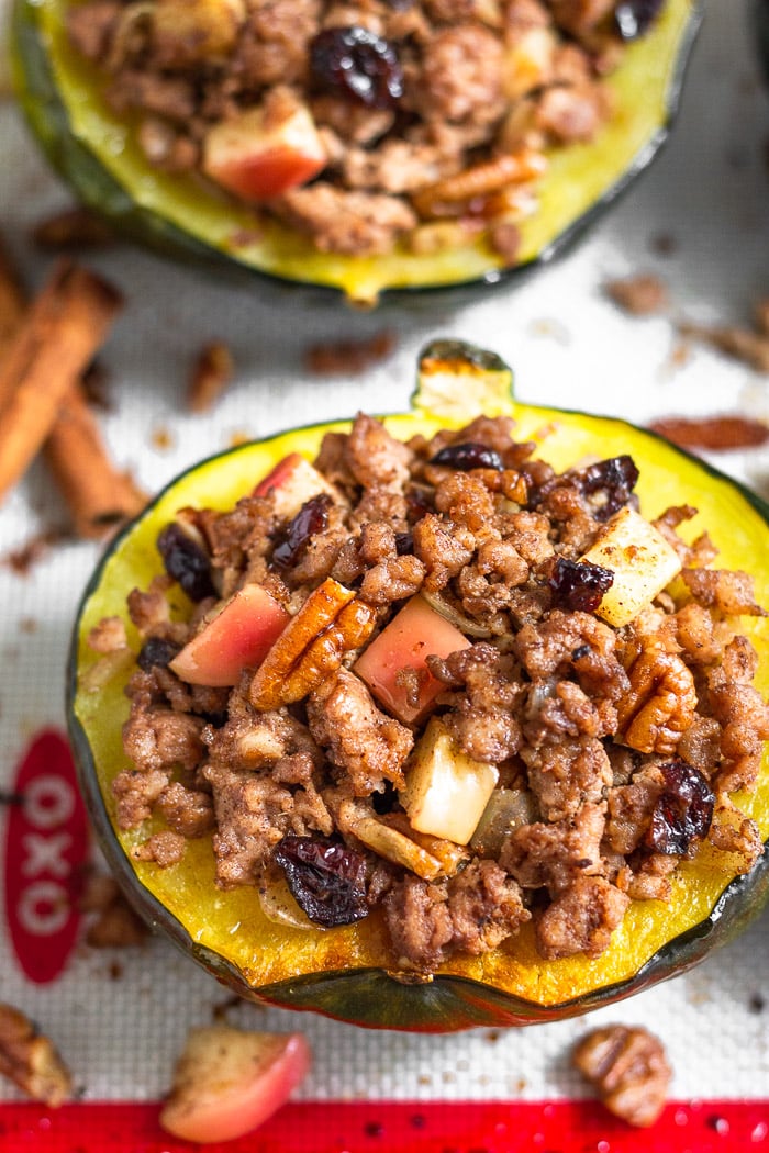Sausage and apple stuffed acorn squash on a baking sheet with the filling scattered around them,