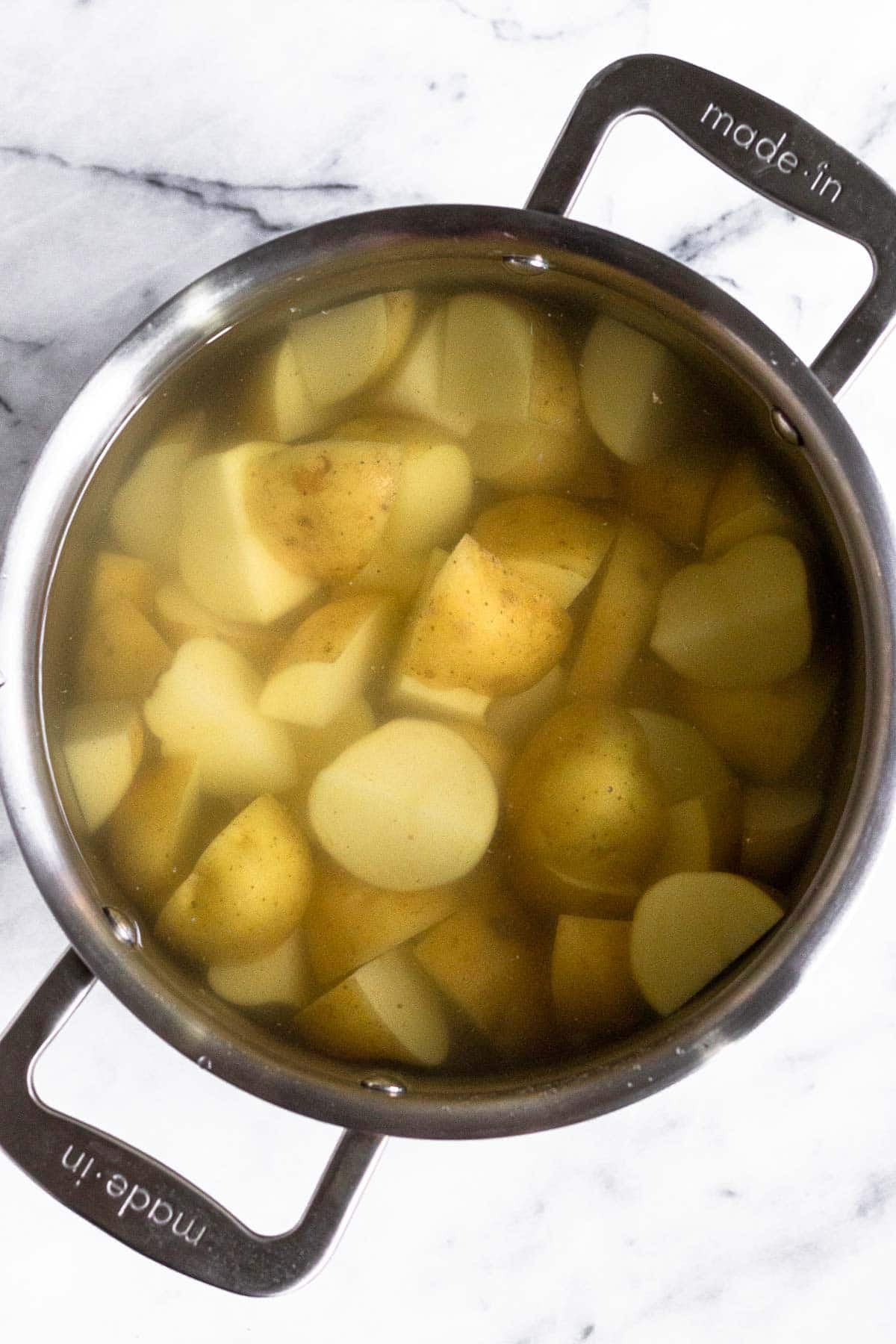 Cut up white potatoes in a pot filled with water.