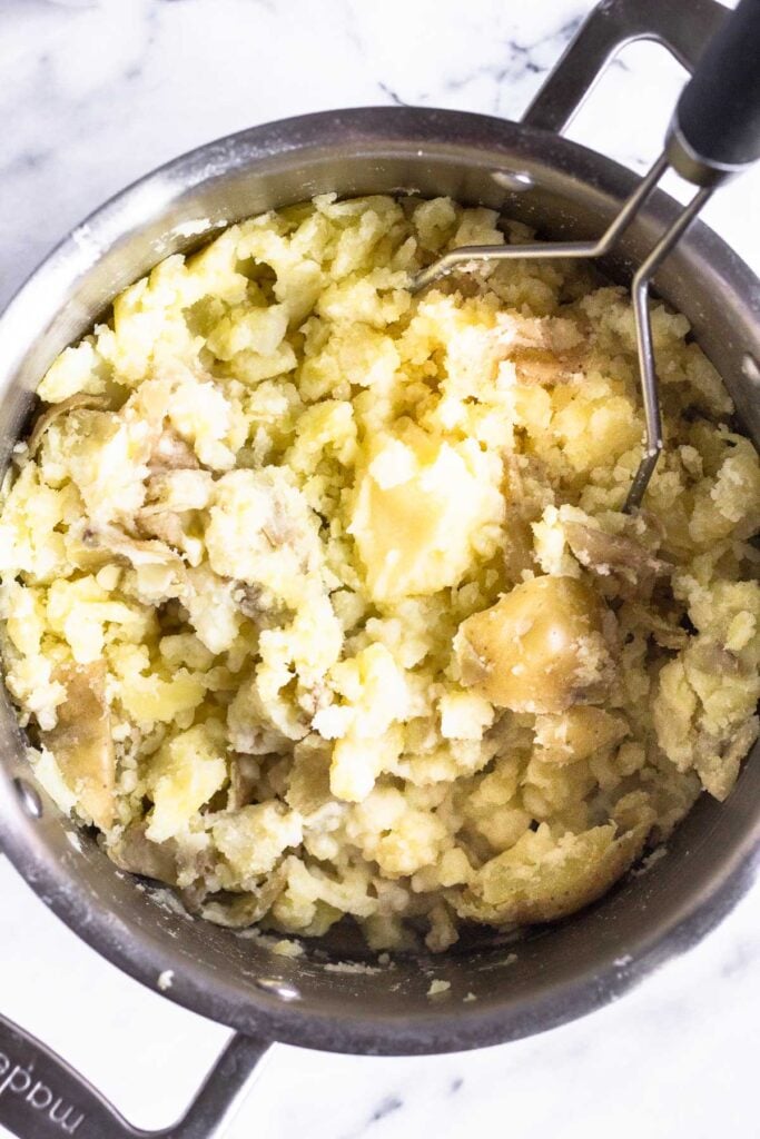 Potatoes that are partially mashed in a large pot.