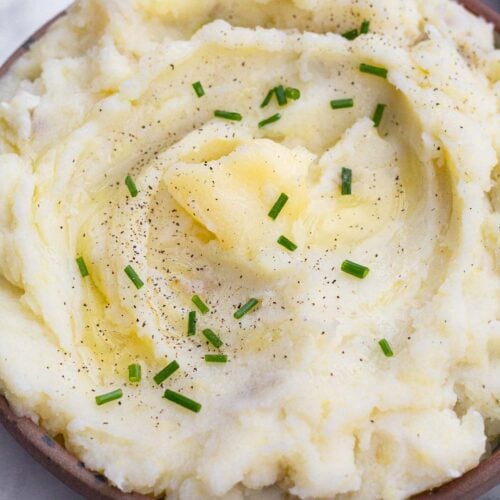 Dairy free mashed potatoes in a bowl. They are topped with ghee, chives, and pepper.