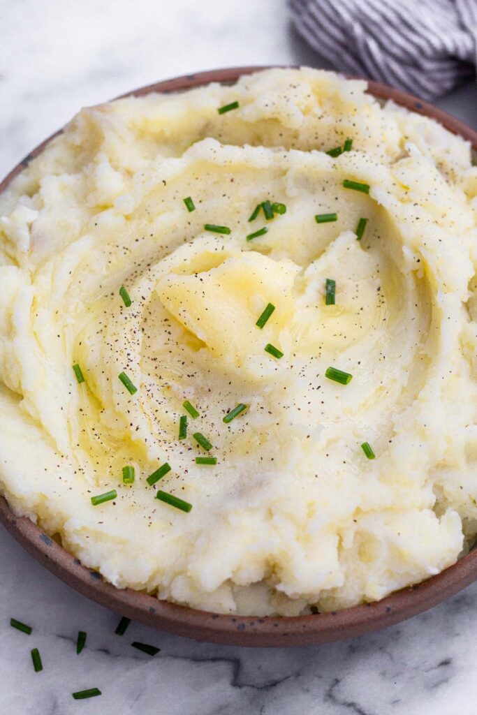 Dairy free mashed potatoes in a bowl. They are topped with ghee, chives, and pepper.