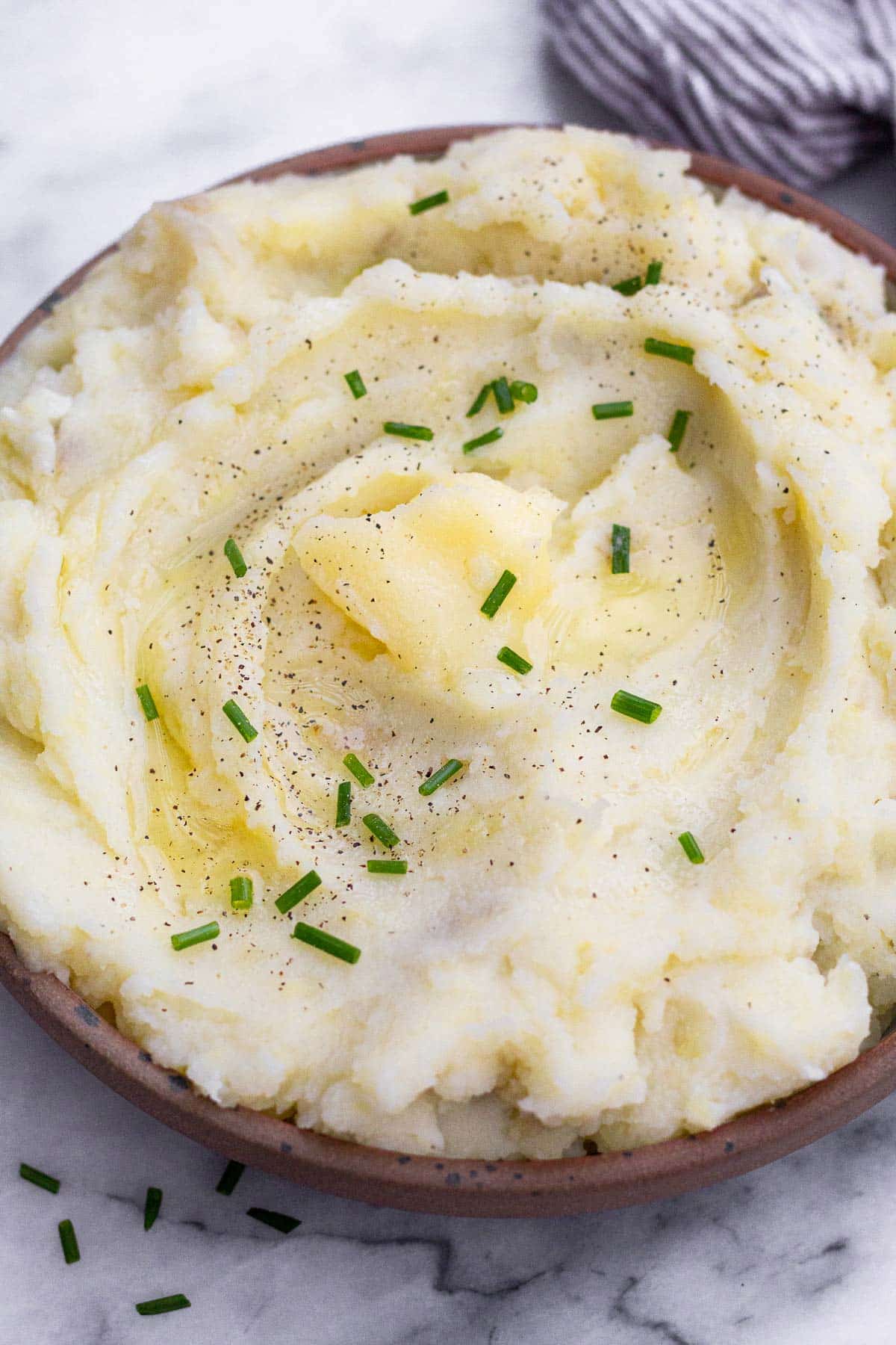 Dairy free mashed potatoes in a bowl. They are topped with ghee, chives, and pepper.