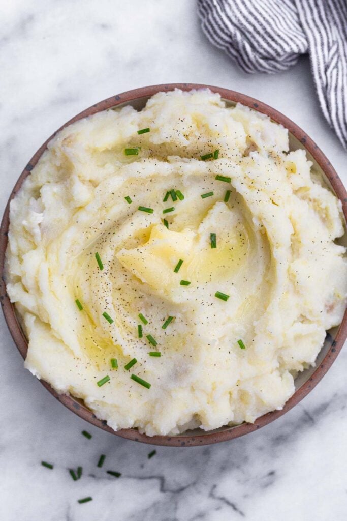 Dairy-free mashed potatoes topped with ghee, chives, and pepper in a bowl.