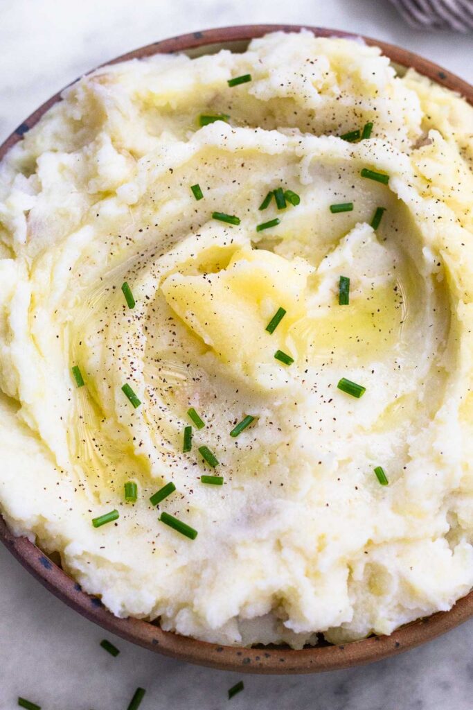 Healthy mashed potatoes in a bowl topped with ghee, chives, and pepper.