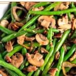 Green beans and mushrooms with bacon and fried onions in a white casserole dish.