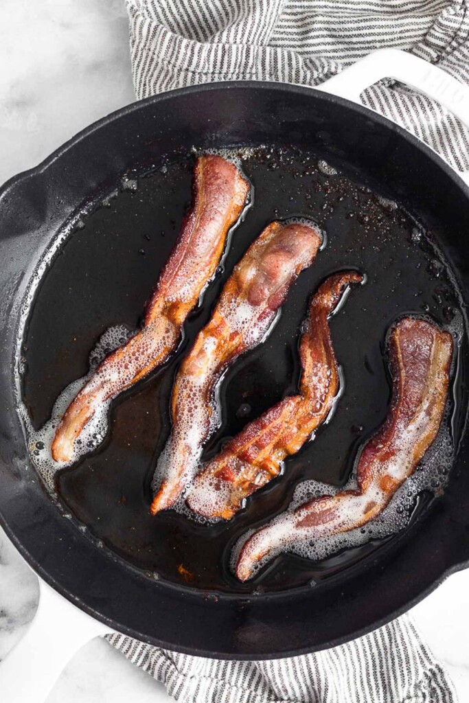 Large cast iron skillet with 4 pieces of fried bacon in it.