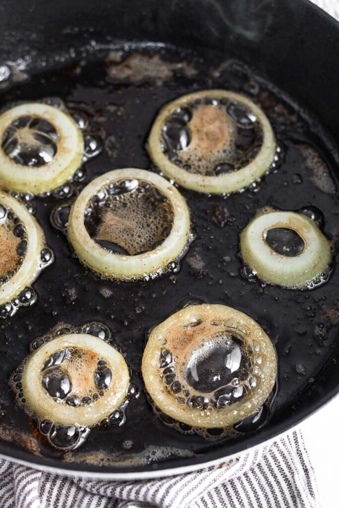 Cast iron skillet with onion rings frying in it.