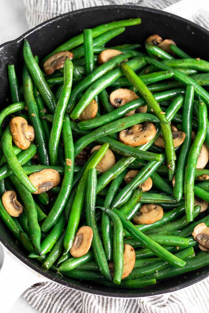 Sautéed green beans and mushrooms in a cast iron skillet. The skillet is sitting on a striped towel.