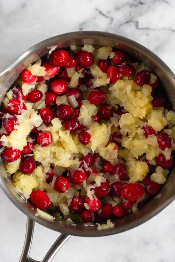 Saucepan filled with whole cranberries and crushed pineapple mixed together.