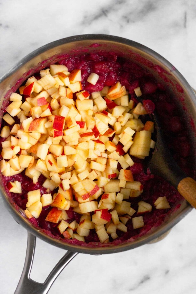 Pot filled with cooked down cranberries and pineapple with diced apple on top.
