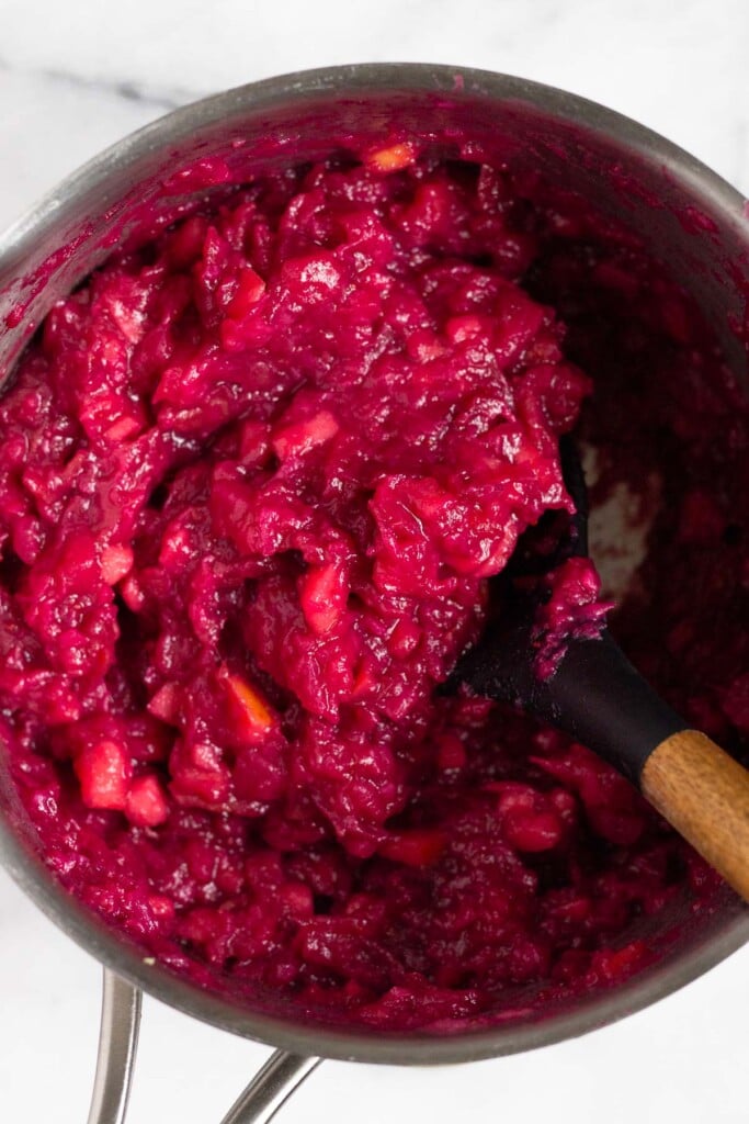 Close up of homemade cranberry sauce in a pot with large stirring spoon in it.