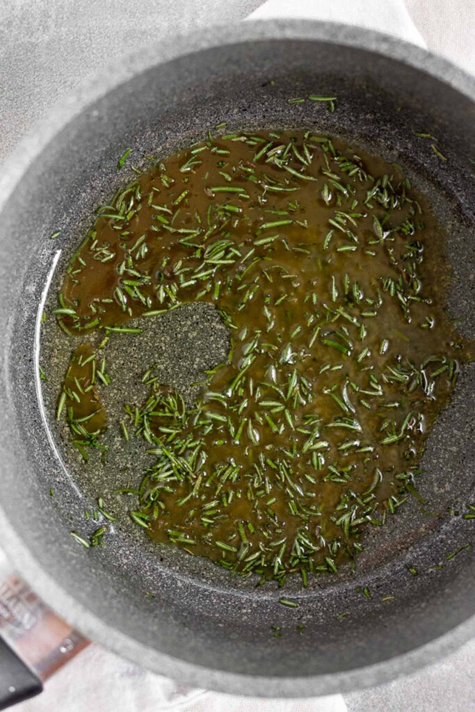 A saucepan filled with coconut oil, honey, and chopped fresh rosemary.