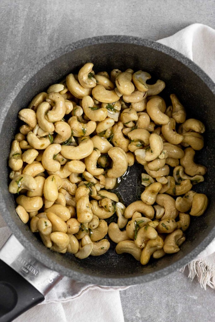 A small pot filled with cashews that are mixed with a mixture of honey, coconut oil, and rosemary.