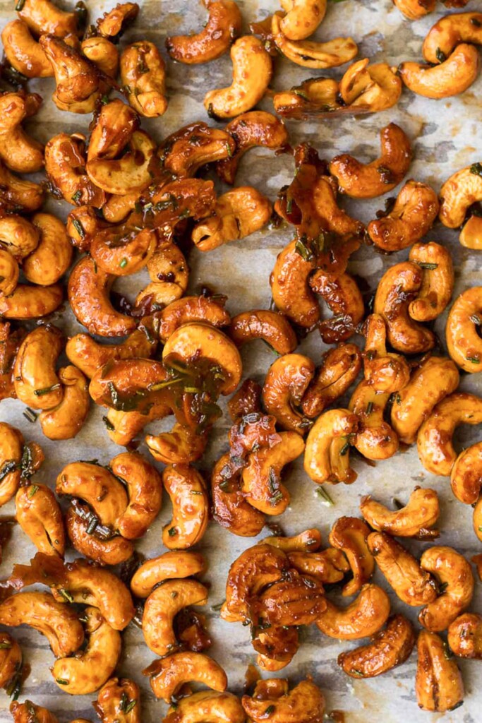Sheet pan of honey roasted cashews topped with rosemary.