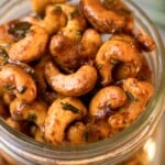 Close up overhead shot of honey roasted cashews in a glass jar. In the background is a sprig of fresh rosemary.