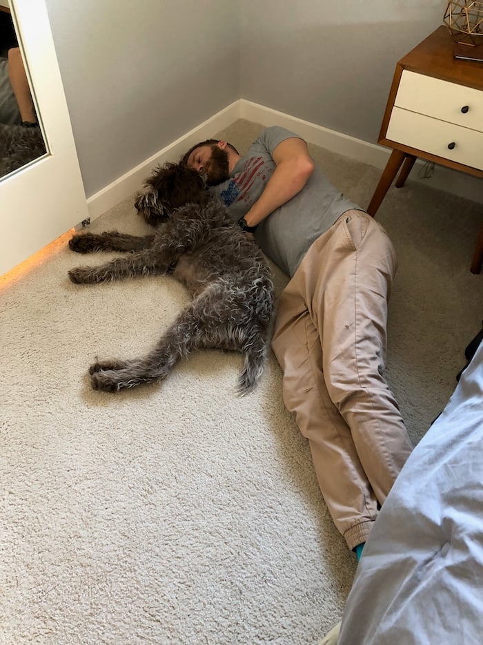 A man and a puppy laying on the ground snuggling.