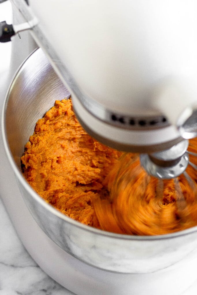 Stand mixer whisking together cooked sweet potatoes, tahini, cinnamon, and roasted garlic.
