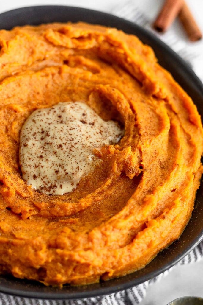 A close up shot of whipped sweet potatoes in a black bowl. They are topped with tahini and cinnamon.