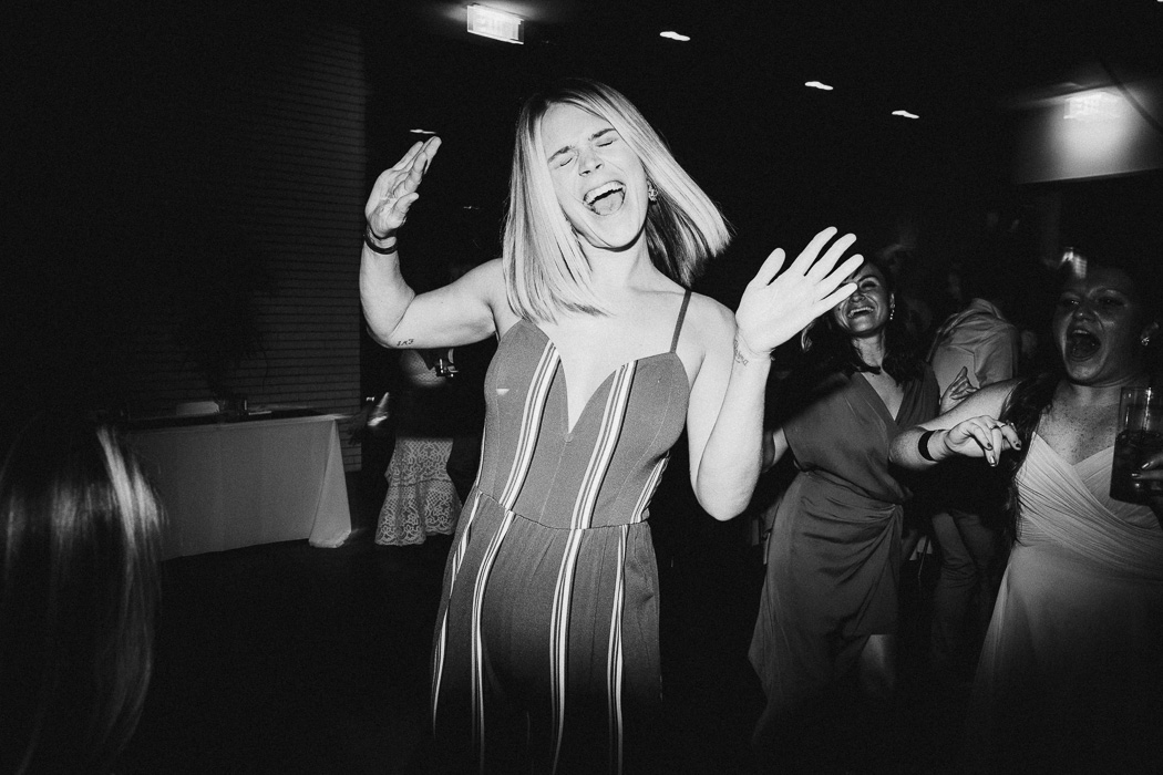 Girl with both her hands up in the air and her eyes shut while she is dancing and singing.