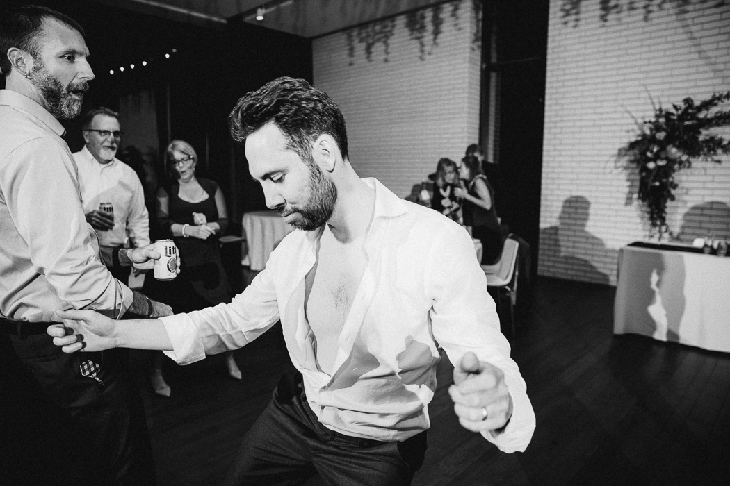 Guy with his shirt halfway unbuttoned dancing at a wedding.