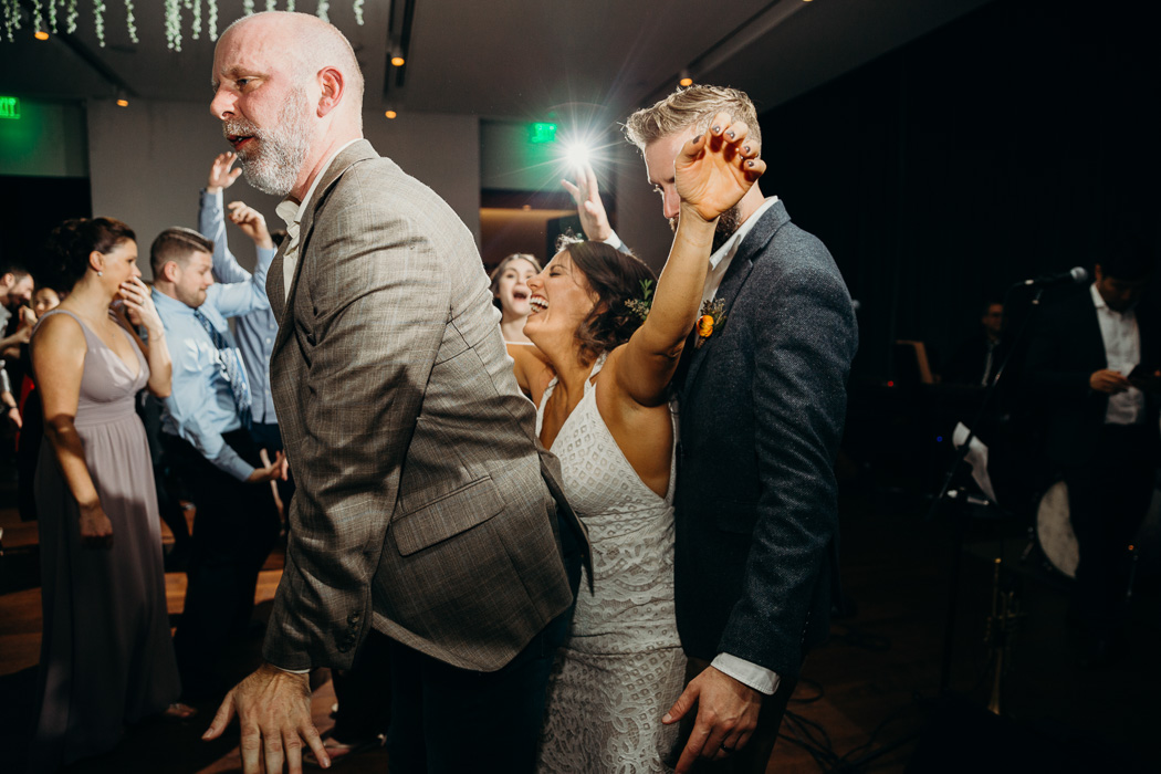 Bride sandwiched in-between the groom an older man and the groom dancing at their wedding.